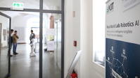 Blick in einen Flur, im Hintergrund unscharf zu erkennen ein humanoider Roboter und Menschen