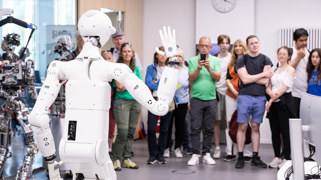 Humanoider Roboter winkt einer Gruppe von interessierten Besuchern zu